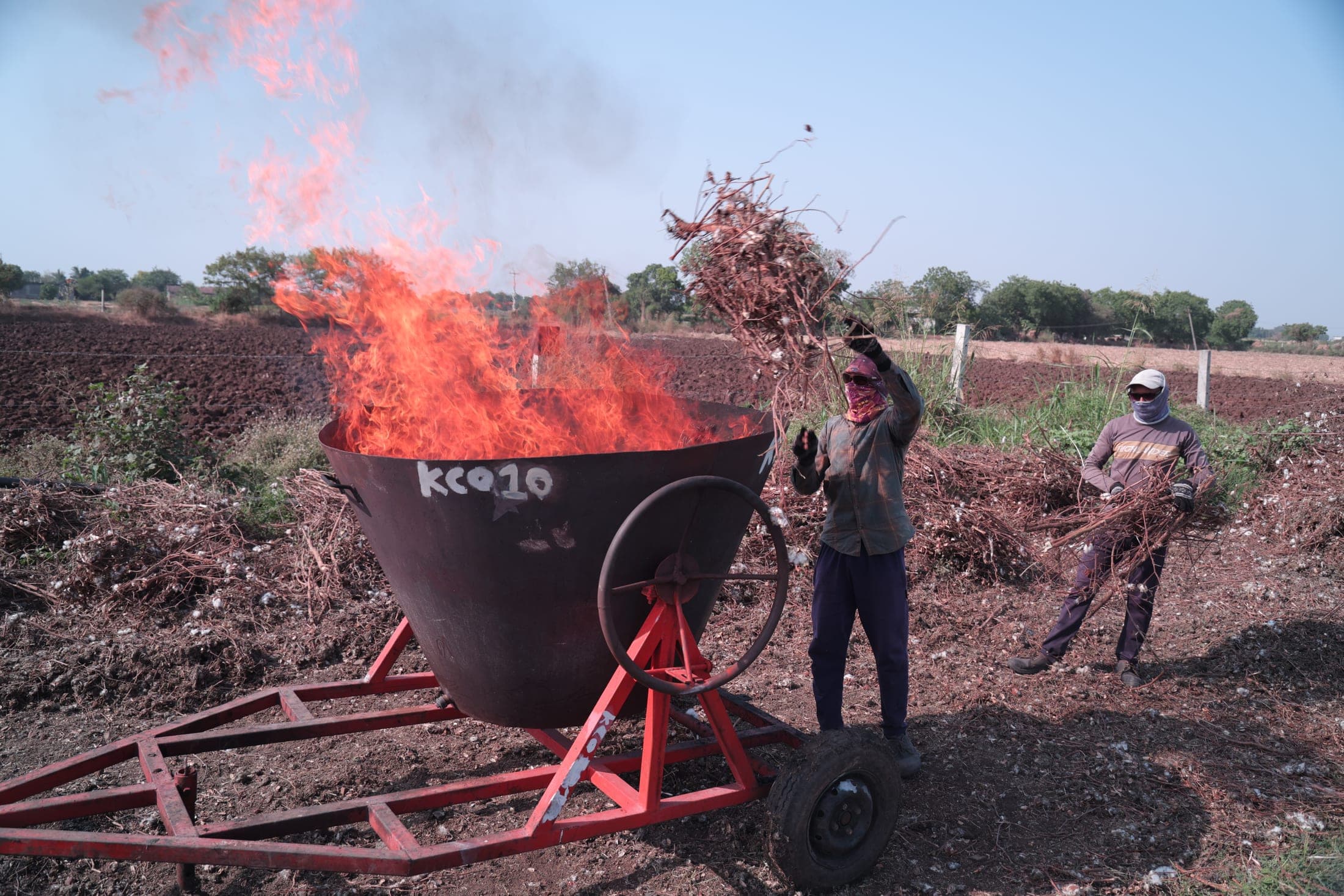A farm worker throws crop residue into a burning cone kiln at the edge of a field
