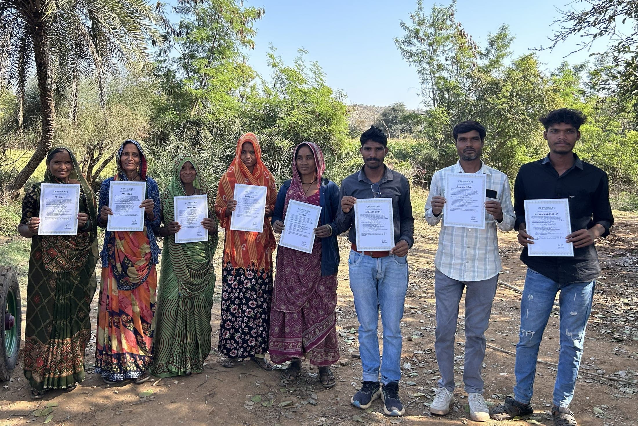 Women and men hold up their training certificates beside a biochar kiln